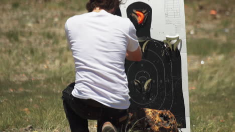 caucasian man crouching, inspects and resets clay target holder on a shooting range