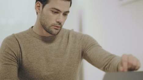 hombre de negocios serio trabajando con una computadora portátil en la cocina.