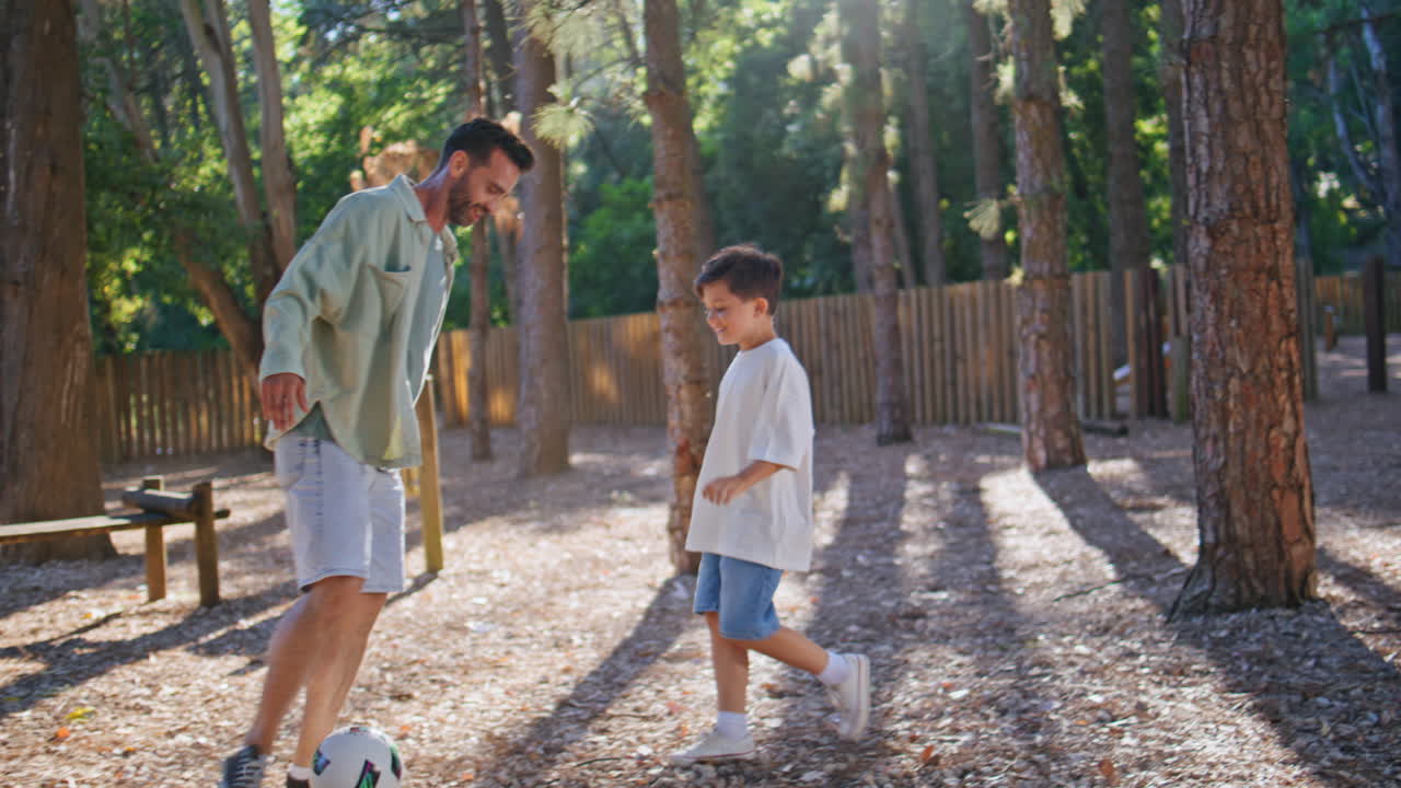 Child father playing ball at summer forest. Man small boy enjoying football game