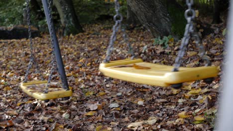 closeup of child's swings in park moving on it's own, static shot