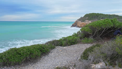 a man on a bicycle is riding along a stony trail that winds its way along untamed coastline of sea