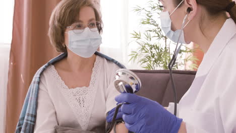 Female-Doctor-Takes-The-Pulse-Of-An-Elderly-Patient-Sitting-On-A-Sofa-4