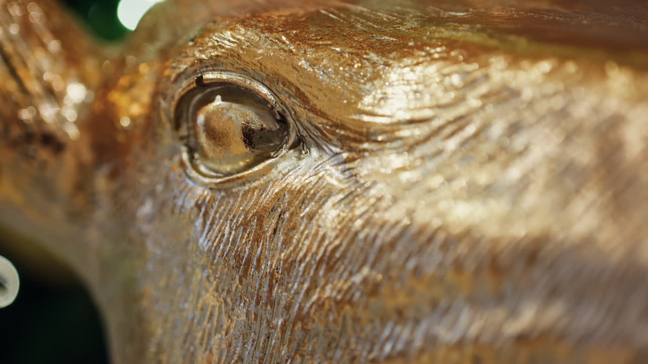 Close up of a golden reindeer sculpture in front of a lighted Christmas tree. Vertical