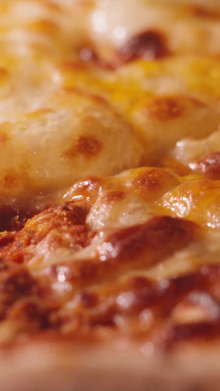 Video verticale: primo piano di delizioso formaggio fuso e filante che bolle su una pizza Margherita al pomodoro.