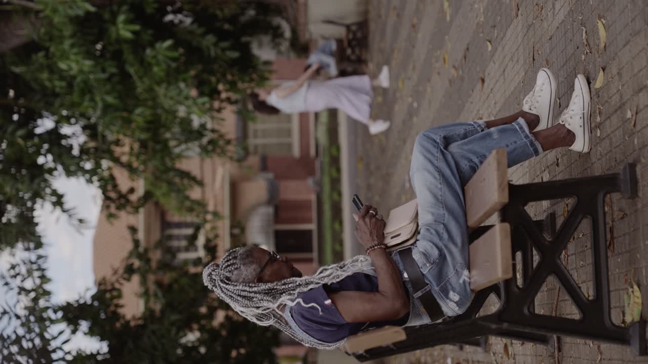 Senior Woman with Braids Relaxing on Park Bench and Using Smartphone