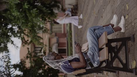 senior woman with braids relaxing on park bench and using smartphone