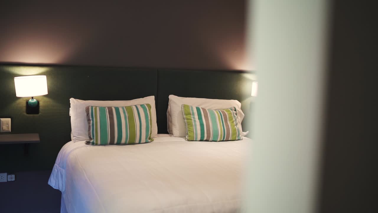 A cozy hotel room with a clean bed, striped pillows, and warm ambient lighting
