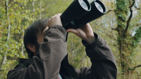 hombre barbudo mirando hacia arriba con binoculares en busca de aves raras en el bosque - cámara lenta