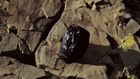 Bolsa-De-Basura-Negra-Yacía-En-Una-Playa-Rocosa