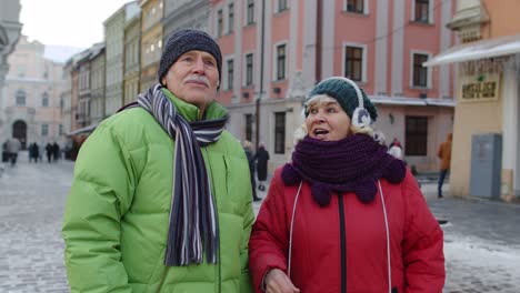 Elderly-senior-man-woman-tourists-talking,-gesturing-in-old-city,-holidays-vacation-trip-concept