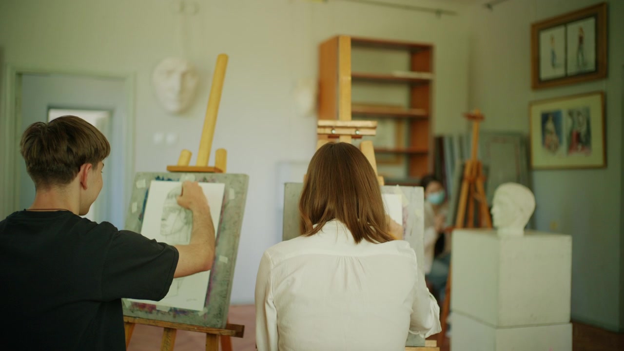 Vista posteriore di studenti concentrati a disegnare ai cavalletti in un'aula di studio d'arte.