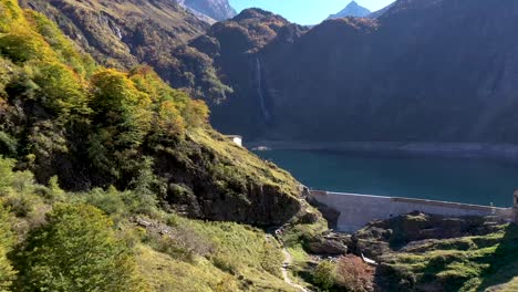 lac d'oô artificial lake in the french pyrenees with hikers standing near the dam wall on a ridge, aerial approach shot