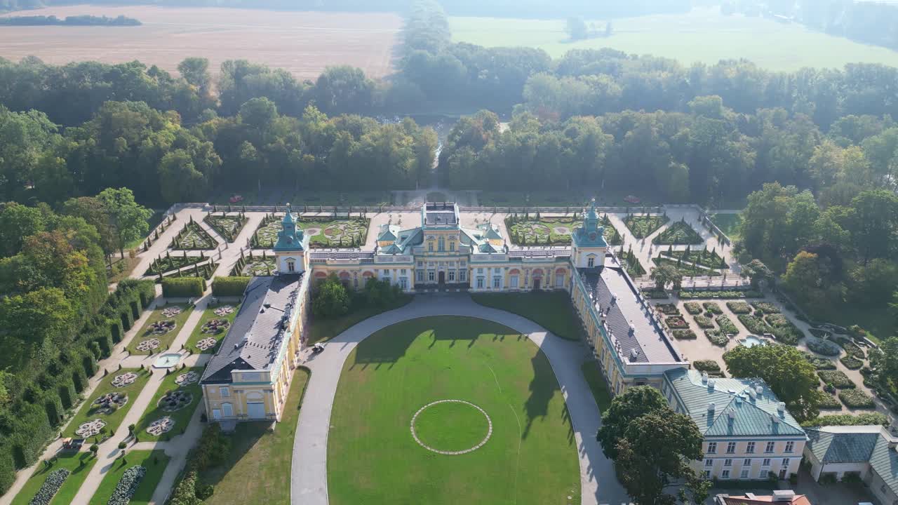Stunning drone view of Wilanów Palace in Warsaw with ornate baroque facade, colorful roof, and vast landscaped gardens bathed in soft morning light