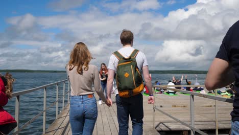 casal caminhando em um cais ao lado de um lago com pessoas relaxando em uma doca flutuante