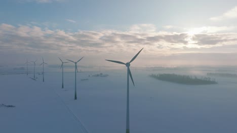 aerial establishing view of wind turbines generating renewable energy in the wind farm, snow filled countryside landscape with fog, sunny winter evening, golden hour light, wide drone orbiting shot