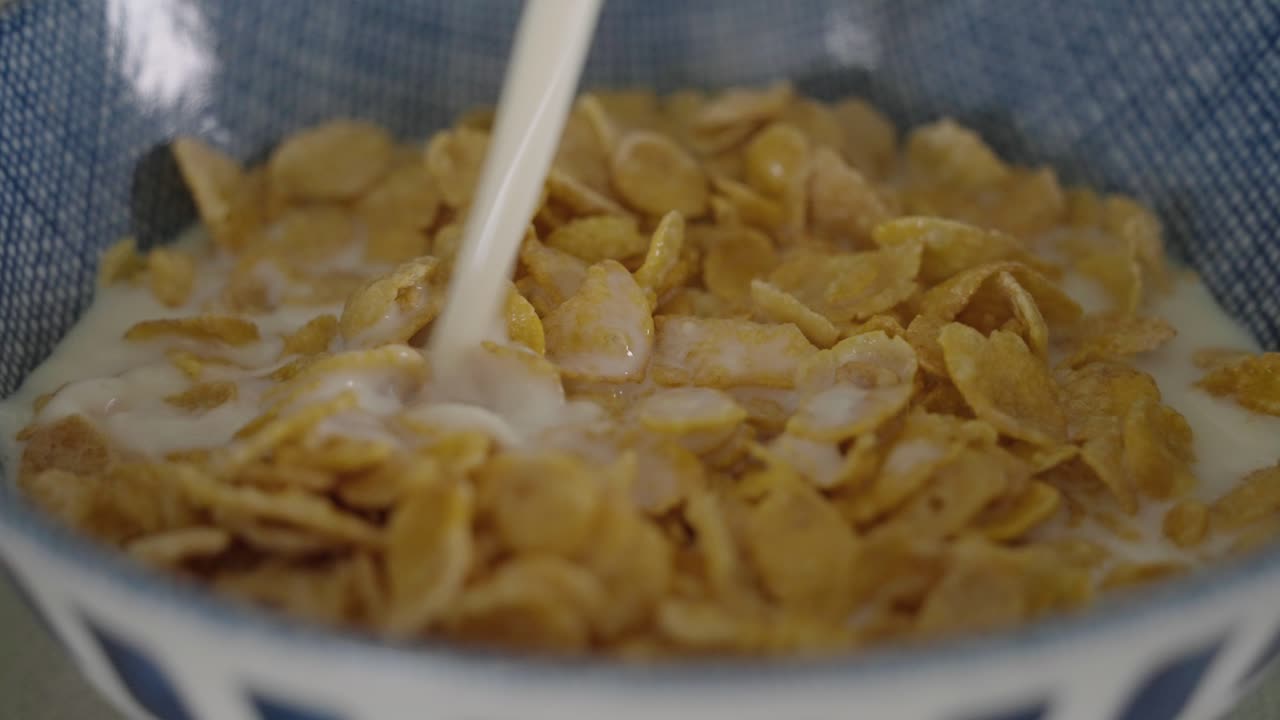 Versare il latte in una ciotola di croccanti corn flakes in una grande ciotola blu, al rallentatore.