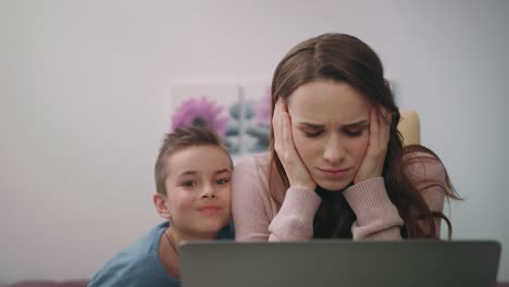 Busy-mom-embrace-son-while-working-on-laptop-computer-at-home