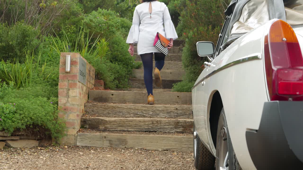 스타킹과 부츠를 신고 빈티지 자동차를 지나 농장의 계단을 오르는 젊은 아가씨