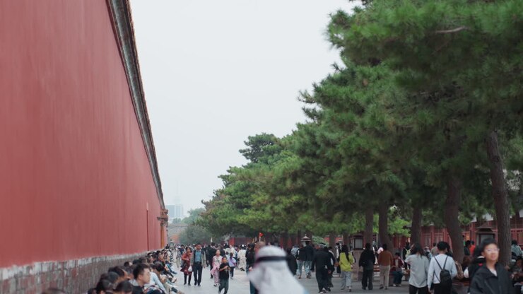 Bustling asian visitors along red wall, street vendors and souvenir stalls, cameras flashing and backpacks moving, fastpaced crowds with guidebooks, vibrant urban travel energy under grey sky
