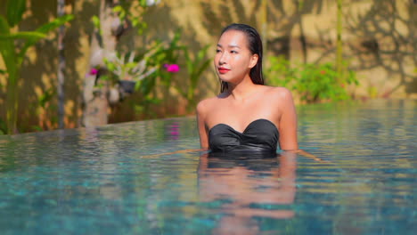 Woman-walking-inside-swimming-pool-and-smooth-her-wet-hair-with-both-hands-at-sunset,-slow-motion-Bali