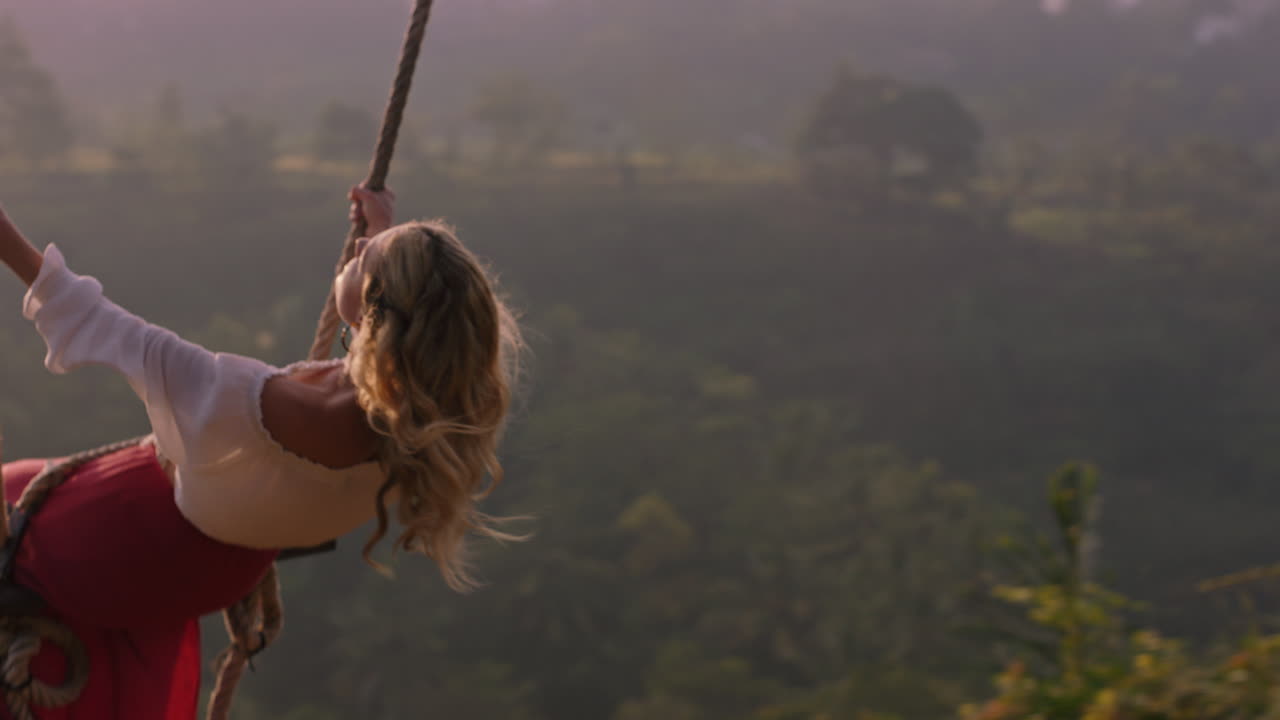 hermosa mujer balanceándose sobre la selva tropical al amanecer sentada en el columpio divirtiéndose disfrutando de la libertad en un estilo de vida de vacaciones exóticas en cámara lenta