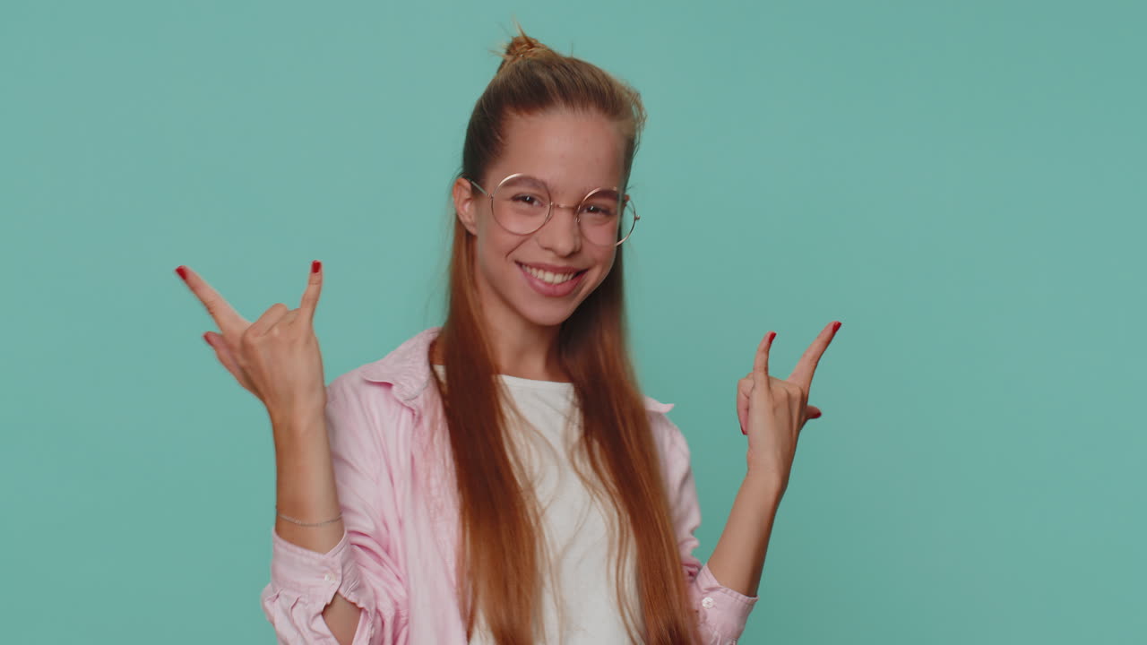 웃고, 기하고, 기하며, 예쁜 소녀가 록 앤 롤 제스처를 보여주고, 춤을 추고, 감정적으로 성공을 기합니다.