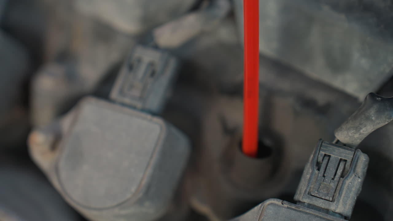 Extreme close up of car engine showing red dipstick fully reinserted after oil level check during cold weather vehicle maintenance with snow-covered background