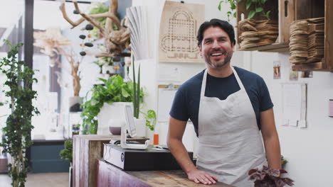 portrait of smiling male sales assistant standing behind sales desk of florists store