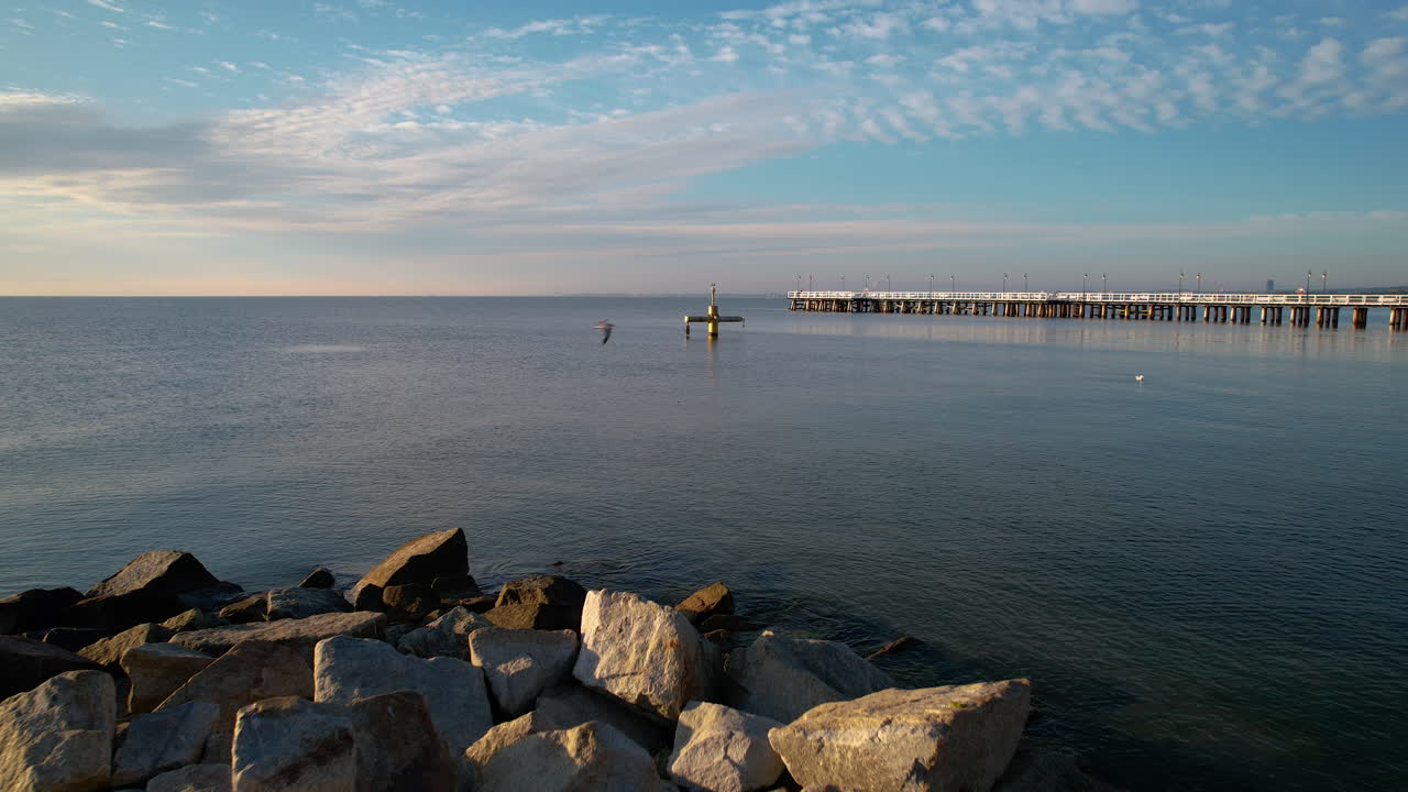 el muelle de orlowo y la playa de arena rocosa al amanecer en gdynia, polonia - retroceso aéreo revelador