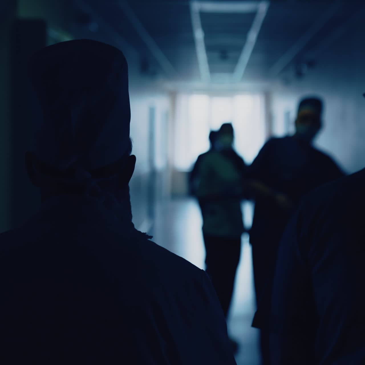 Silhouette of doctors moving to the operating room. Medical workers wearing medical uniform walking in hospital corridor. Back view