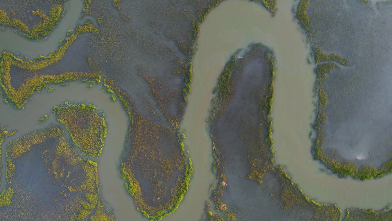 An overhead drone shot view panning out of ocean marshland with a river going through it.