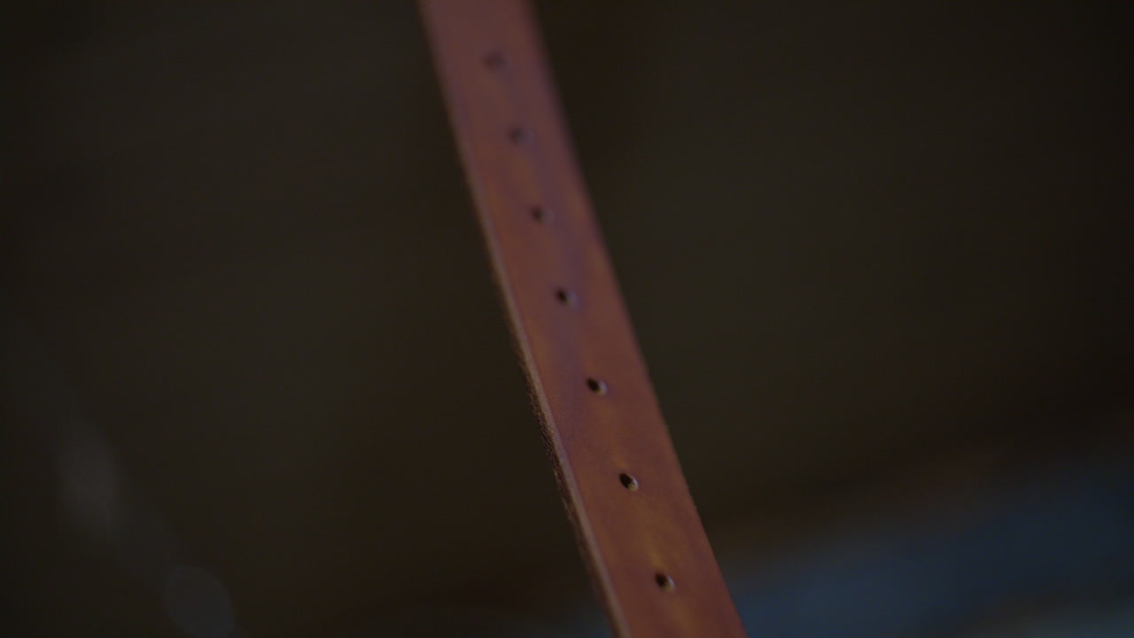 A detailed view of a dyed leather strap with evenly punched holes, suspended for drying after the crafting process.