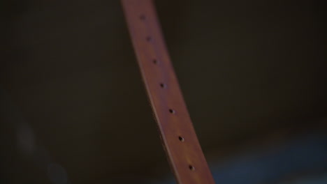 a detailed view of a dyed leather strap with evenly punched holes, suspended for drying after the crafting process.