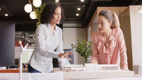 diverse female architects discussing architectural model of building at work, in slow motion