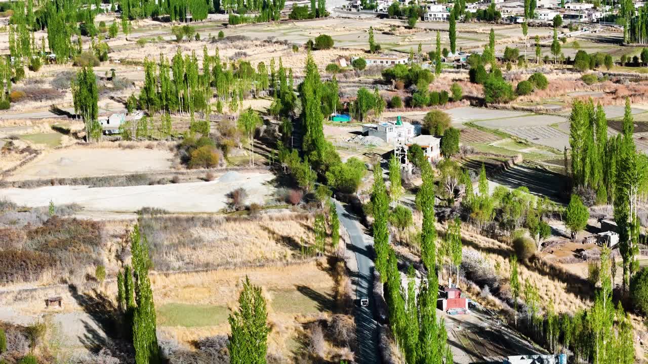 Aerial drone shot following a road cutting through the dramatic and wide landscapes of Nubra Valley.