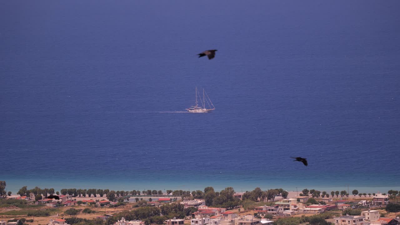View Of Traditional Sail Boat With Mast Off In Distance In The Mediterranean Sea Off Rhodes With Birds Flying Past