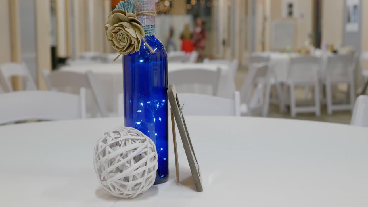 clip de stock del día de la boda de botella de vino decorativa y bola de hilo con decoraciones de marco de imagen en la mesa de recepción con niños corriendo jugando en el fondo
