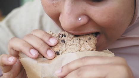 close up of a woman's face as she bites into a chocolate chip cookie.