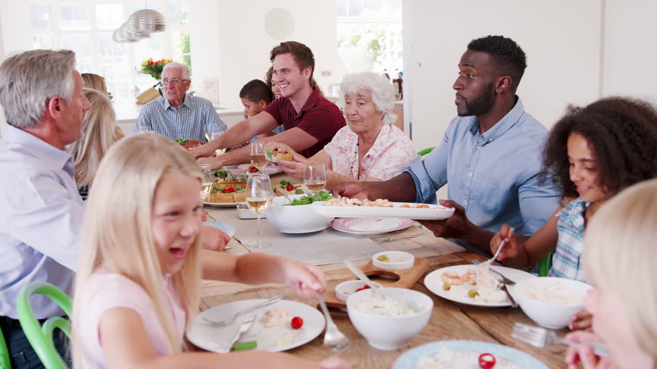 foto em câmera lenta de família e amigos de várias gerações sentados à mesa e desfrutando de uma refeição juntos
