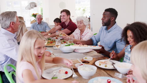 Toma-En-Cámara-Lenta-De-Familiares-Y-Amigos-De-Varias-Generaciones-Sentados-Alrededor-De-La-Mesa-Y-Disfrutando-De-Una-Comida-Juntos