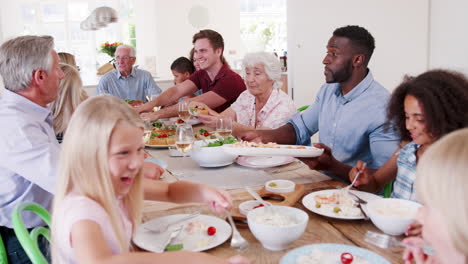 slow motion shot of multi-generation family and friends sitting around table and enjoying meal together