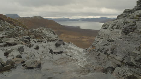 Water-flows-in-slow-motion-over-the-edge-with-lake-and-mountains-in-the-backround