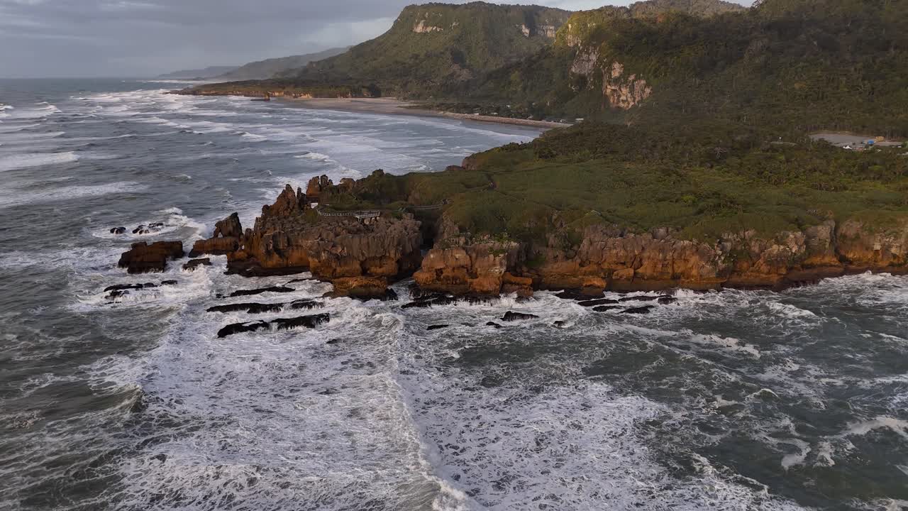 Pancake Rocks e potenti onde oceaniche al tramonto sulla costa occidentale della Nuova Zelanda. Ripresa aerea con movimento all'indietro, spazio per il testo.