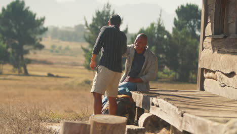 dos amigos varones de vacaciones sentados en el porche de una cabaña de campo bebiendo cerveza juntos
