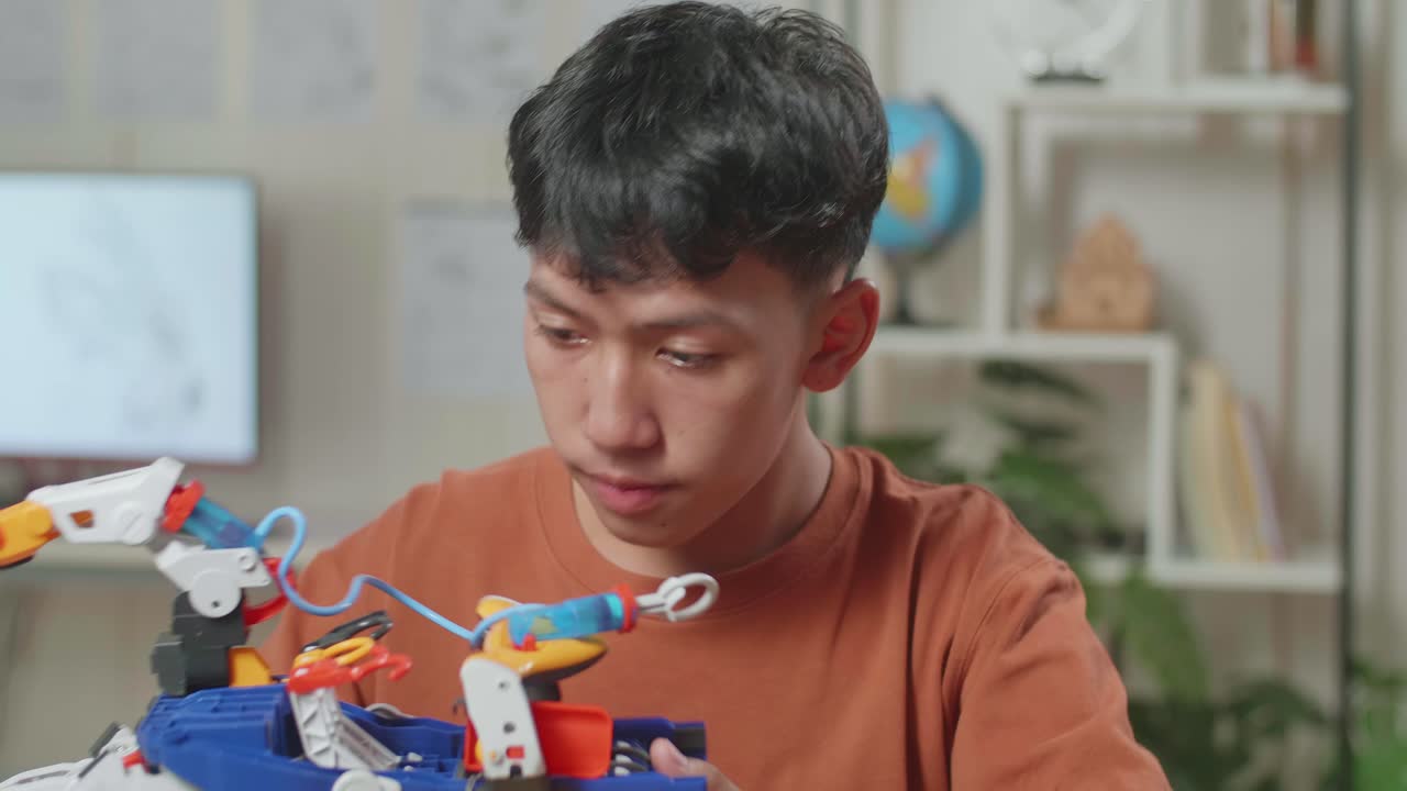 primer plano de un niño asiático con una mano de cyborg sonriendo a la cámara mientras trabaja en una computadora portátil en casa