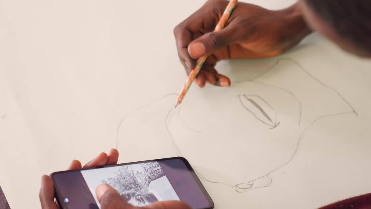 Black man practicing portrait lines with phone guide. Hands hold phone showing grayscale reference while pencil traces facial contours on paper, classroom vibe, patient study session with precise