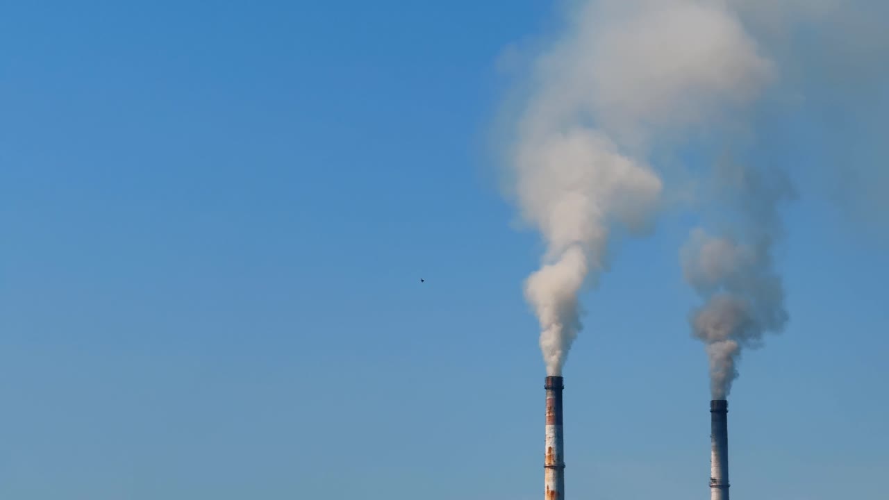 Il fumo si alza dai camini delle fabbriche in un cielo azzurro durante le ore diurne. Il fumo della fabbrica si riversa da due alti camini nel cielo azzurro in un tipico ambiente urbano.