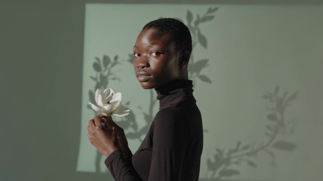 Donna con dolcevita nero che si gira dopo aver osservato una magnolia, guardando la telecamera tra l'ombra delle piante