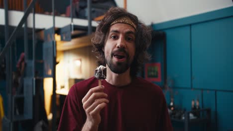 Happy-man-with-patlaty-hair-with-a-beard-in-a-red-t-shirt-eating-ice-cream-looks-at-the-camera-and-smiles-In-a-cozy-room