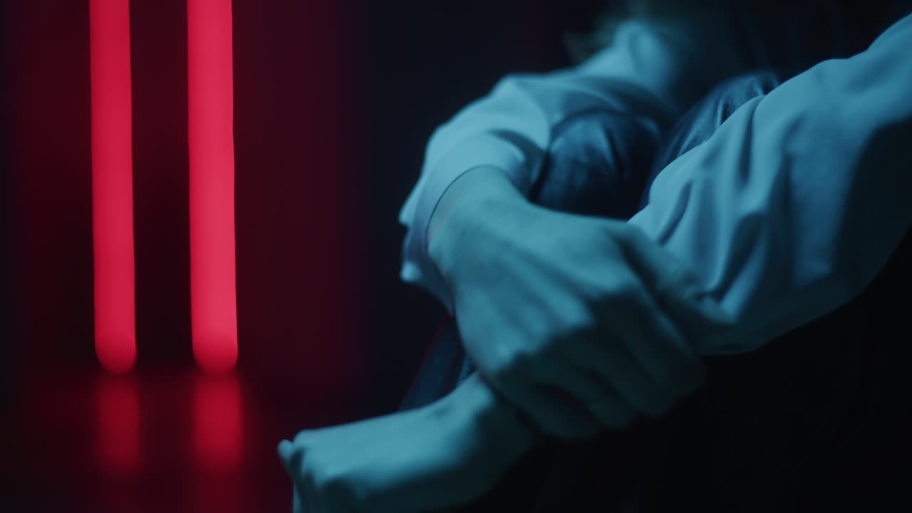 Person Sitting in Darkness with Neon Light